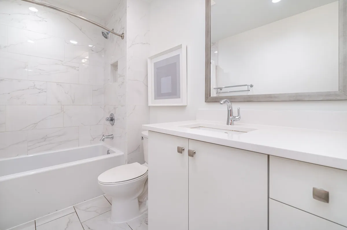 A calming bathroom scene with a bathtub, sink, large mirror, and framed artwork. The atmosphere is tranquil, with soft lighting and simple yet comforting decor, emphasizing relaxation and self-care.