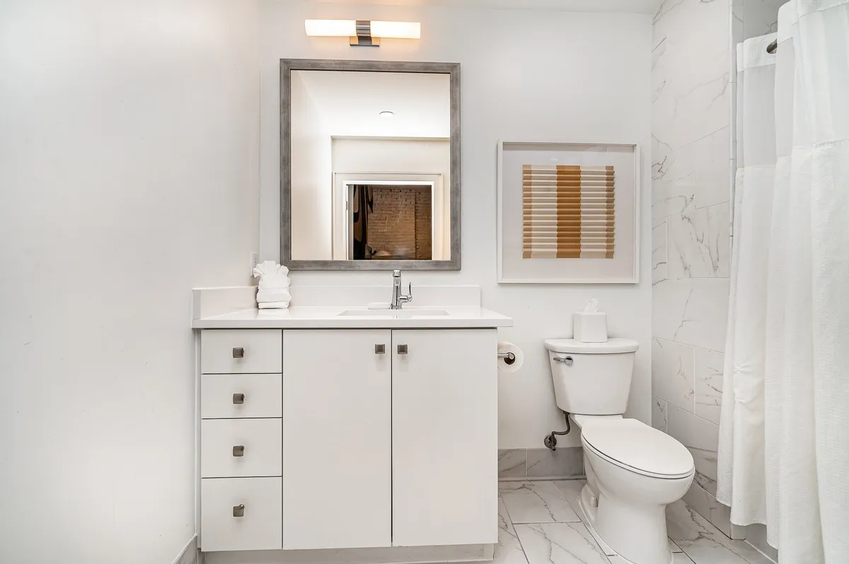 A modern half bathroom featuring a large mirror, contemporary sink, toilet, and stylish wall art. The lighting is fresh and the space feels clean and inviting—perfect for quick freshen-ups.