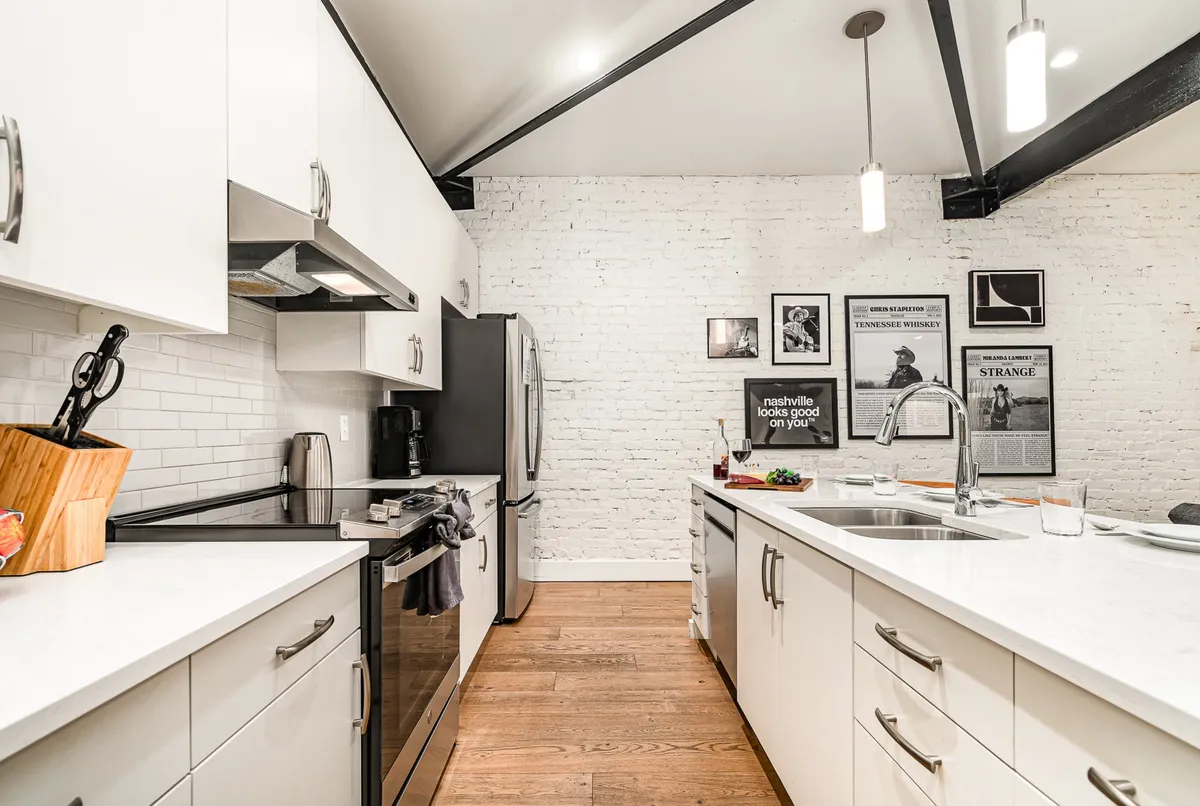 A stylish kitchen with a white brick wall, modern appliances, a kitchen island, and framed art. The island is set up for casual dining or spreading out a feast, and the overall look is inviting and functional.