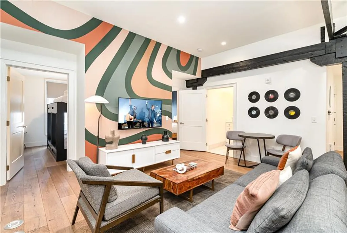 The image showcases a vibrant and inviting living area with a colorful accent wall, a large TV displaying a lively scene, and a wooden coffee table at the center. The room is set up for socializing, relaxing, and watching movies, with comfortable seating arranged to encourage group gatherings and conversation.