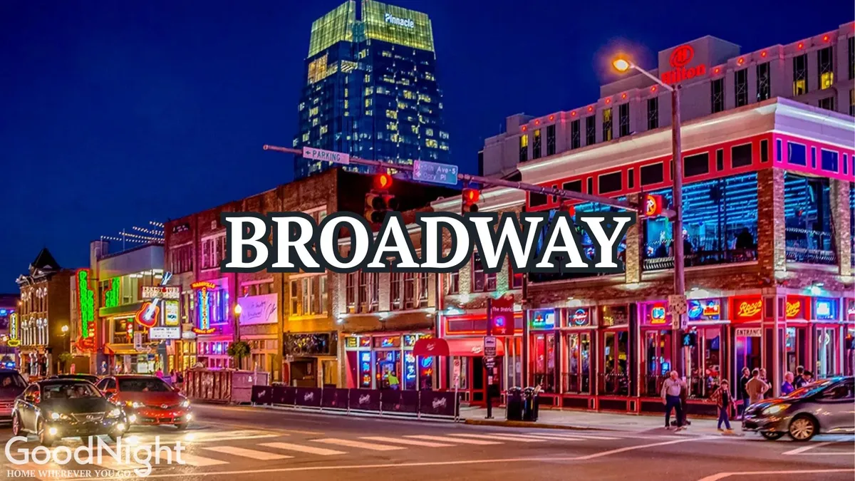 A vibrant nighttime street scene featuring colorful neon signs, a busy street with people walking, and a variety of bars and restaurants. The lively atmosphere is filled with the energy of live music, nightlife experiences, and the festive spirit that defines Broadway in Nashville.